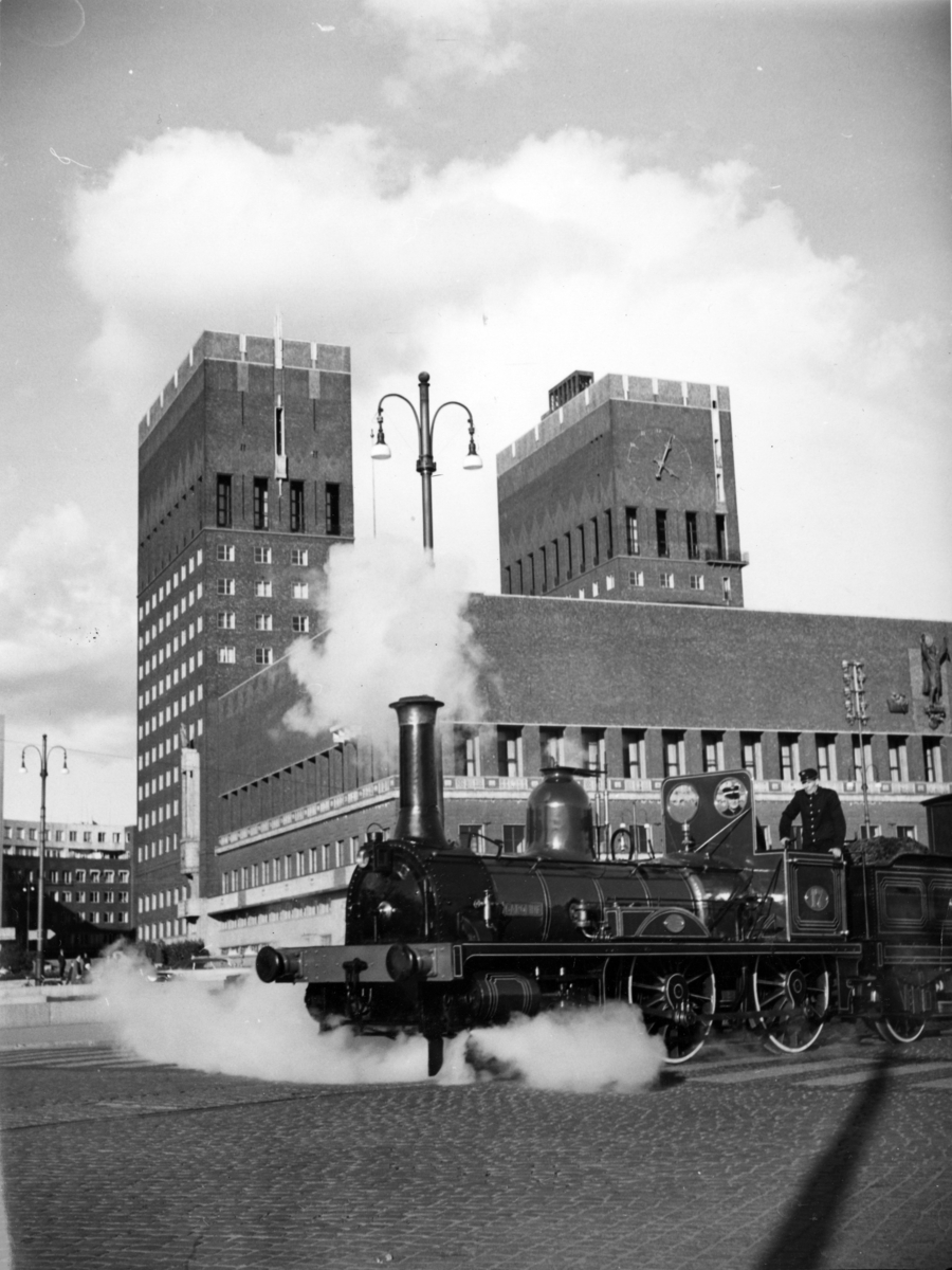 Foto av Rådhuset i Oslo med et lokomotiv i forgrunnen.
