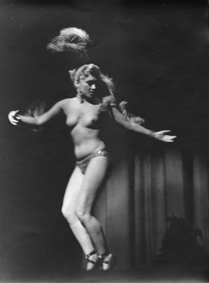 Nesten naken kvinne danser på en scene. Trolig tatt i utlandet. Fotografiet er fra en av fotografene i Oslo Kameraklubb, trolig Erland Rygh eller Sivert Vistaunet. Årstallet 1954 notert på baksiden.