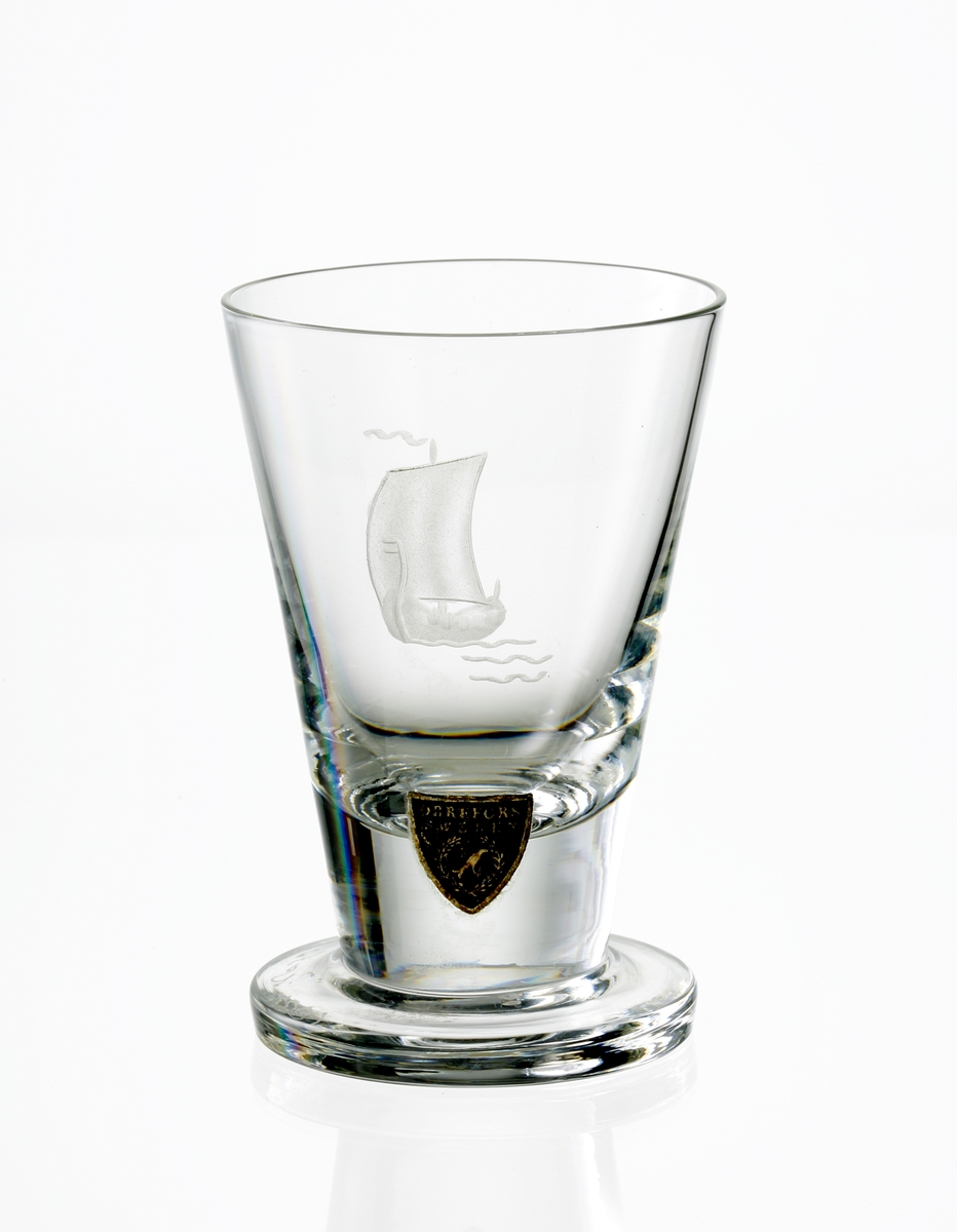 Design: Nils Landberg.
Brännvinsglas. Konande slät kupa med graverat vikingaskepp.
Fabriksmärke: blå botten med guldtext.