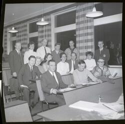 Fotografi av noen menn og kvinner som står og sitter på stol