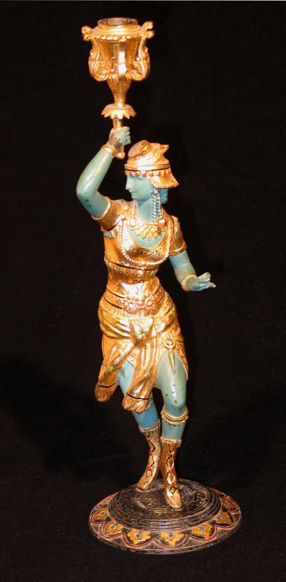 Lysestaken er laget i jern eller bronse. Den forestiller en orientalsk danserinne som står på et rundt fotstykke. Hun holder et skaft som ender i en lysbeholder. Ansiktet og kroppen er malt grønn, mens drakt og sko er gullforgylte.