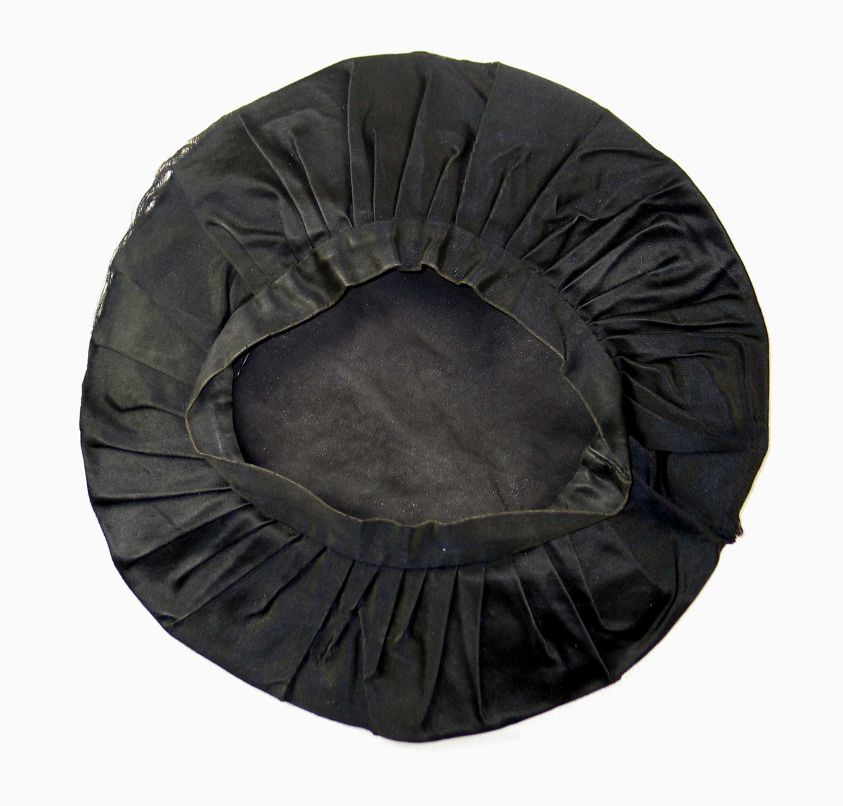 Pull sydd av sirkelrundt stykke silketøy med diam 54 og 46 folder, vendt samme vei, sydd til en tre cm bred og 61 cm lang linning.