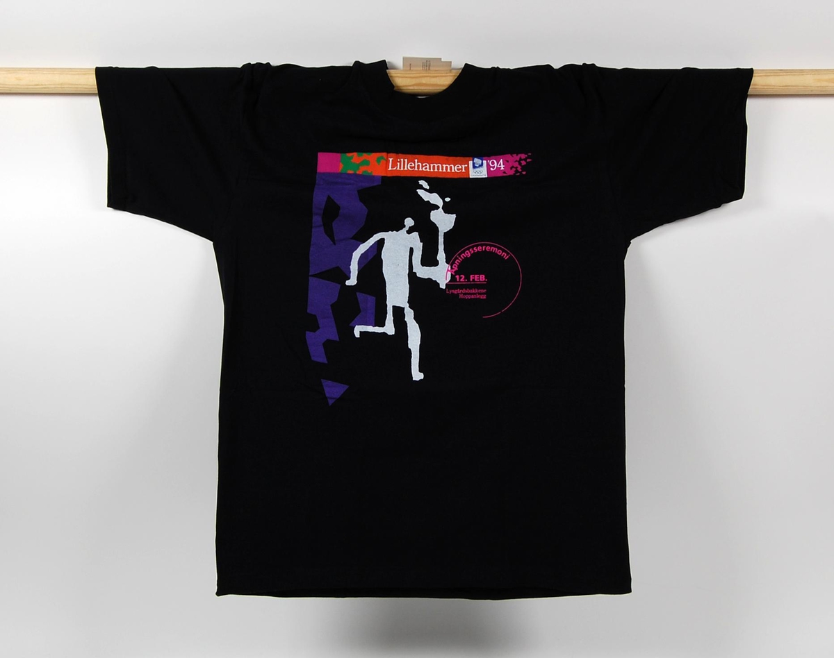 Sort t-skjorte i størrelse L. T-skjorten har motiv av Fakkelmannen. I motivet inngår også et flerfarget krystallmønster. Krystallmønsteret inngikk i LOOCs desigprogram. T-skjorten har også en logo for de olympiske vinterleker på Lillehammer i 1994.
