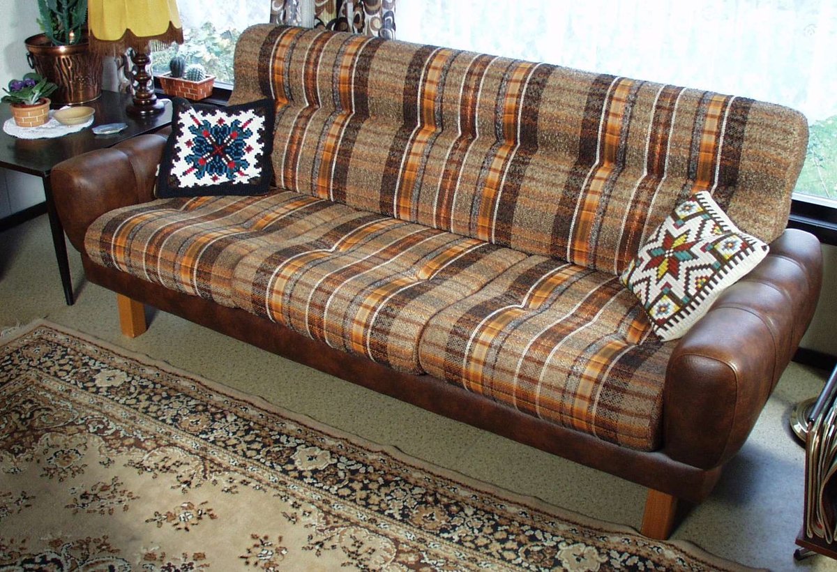 Sofa trukket i brun skai. Putene i rygg og sete er oransje- og brunstripete tekstil.