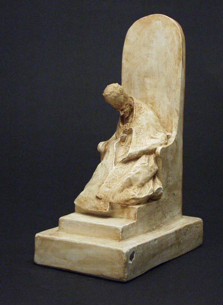 Figur støpt i gips: En mann sittende i høy pavestol på firkantet fotstykke.
