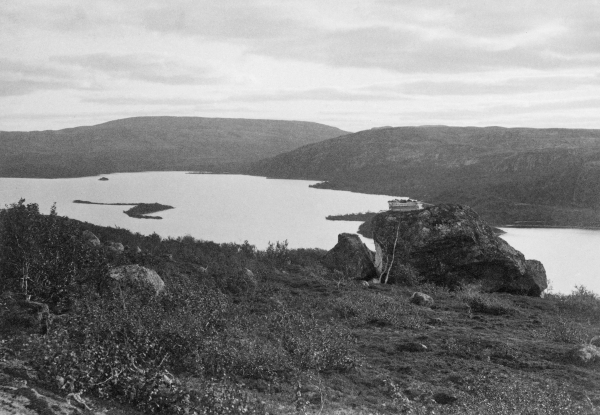 Landskapsfotografi fra Jarfjord i Sør-Varanger.  Bildet er tatt fra en åsrygg med krattskog og en del digre steinblokker.  På den største av dem er det en trekonstruksjon (jfr. DSS. 4045).  I bakgrunnen ses fjorden med et par holmer, samt åsene på motsatt side. 