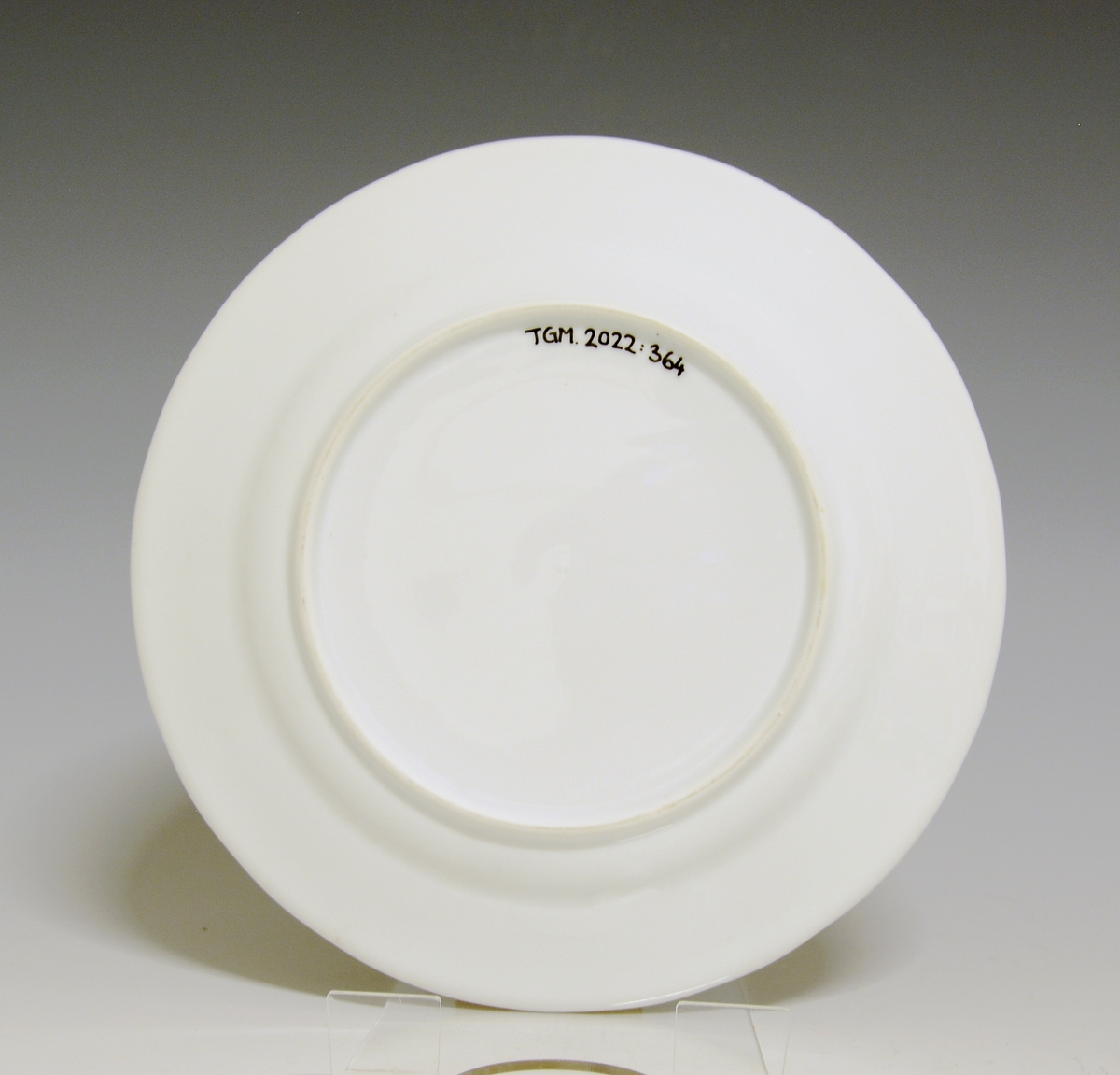 Liten tallerken av porselen. Hvit glasur. Håndmalt underglasurdekor i blått på fanen 
Modell: Victoria, 1800
