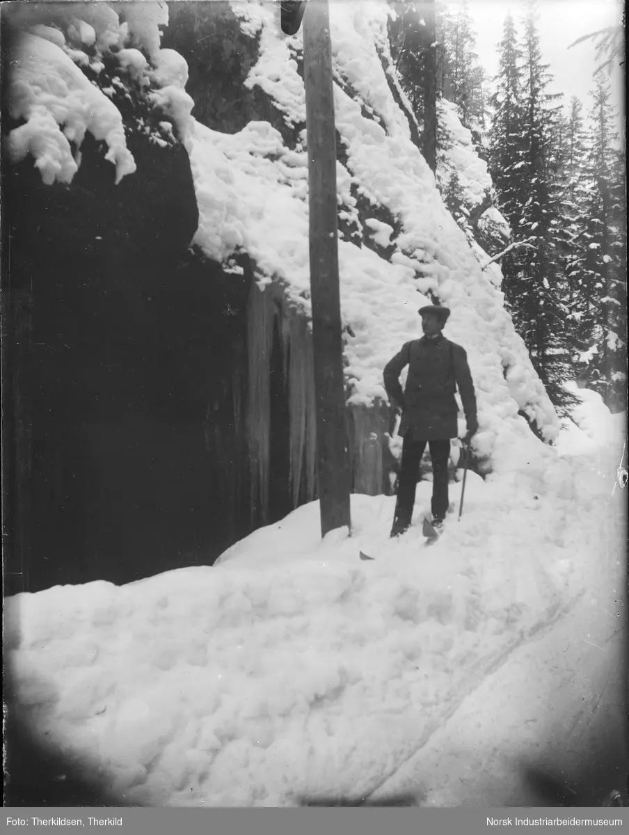 Mann på ski med sekk på ryggen stående ved siden av en telefonstolpe.