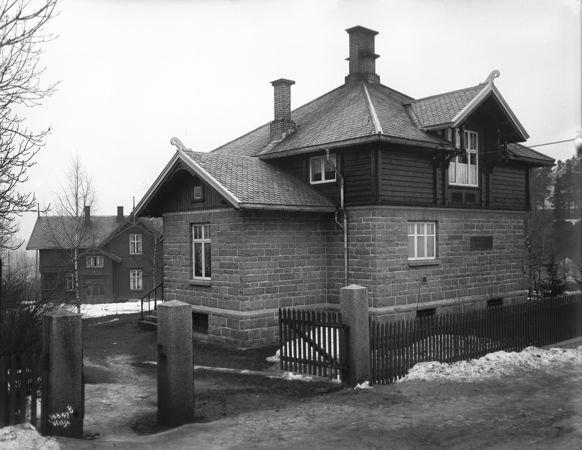 Hus i mur og tre, port og innkjøring fra gaten.  I bakgrunnen ligger et større hus i tre.