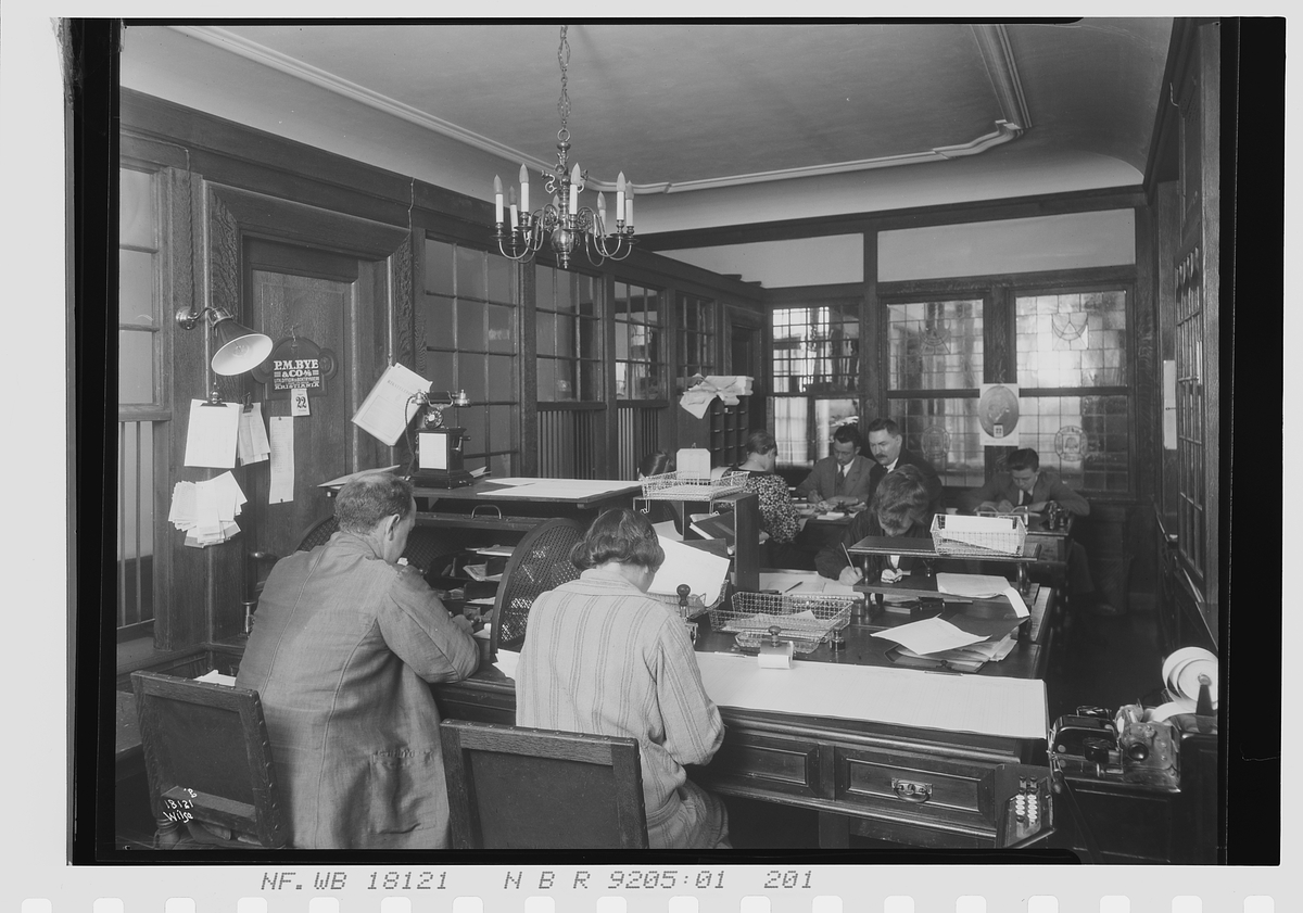 Kvinner og menn sitter om hverandre i et stort kontor, Vinmonopolet. Fotografert 1924.