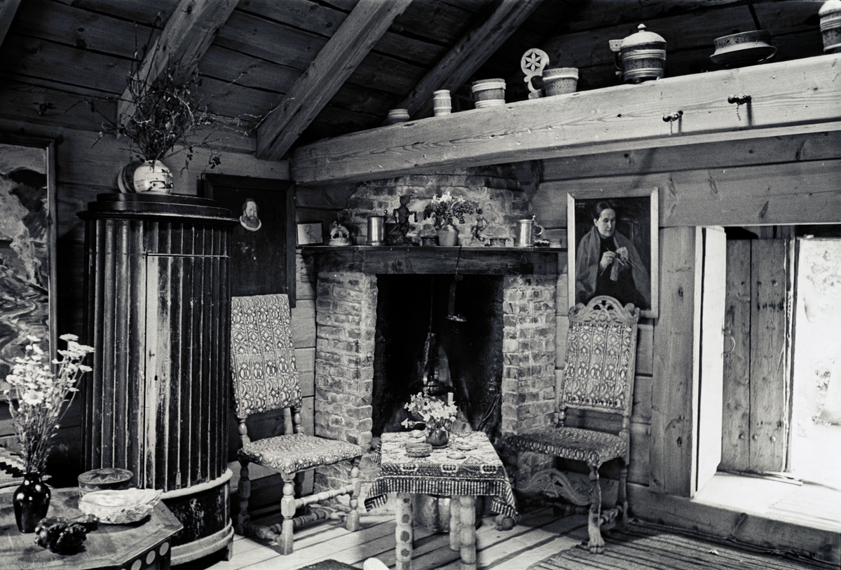 Interiør fra stuen i Astrups hjem, peis i hjørnet, på bjelken over døren står trebutter og tiner av ulike slag.