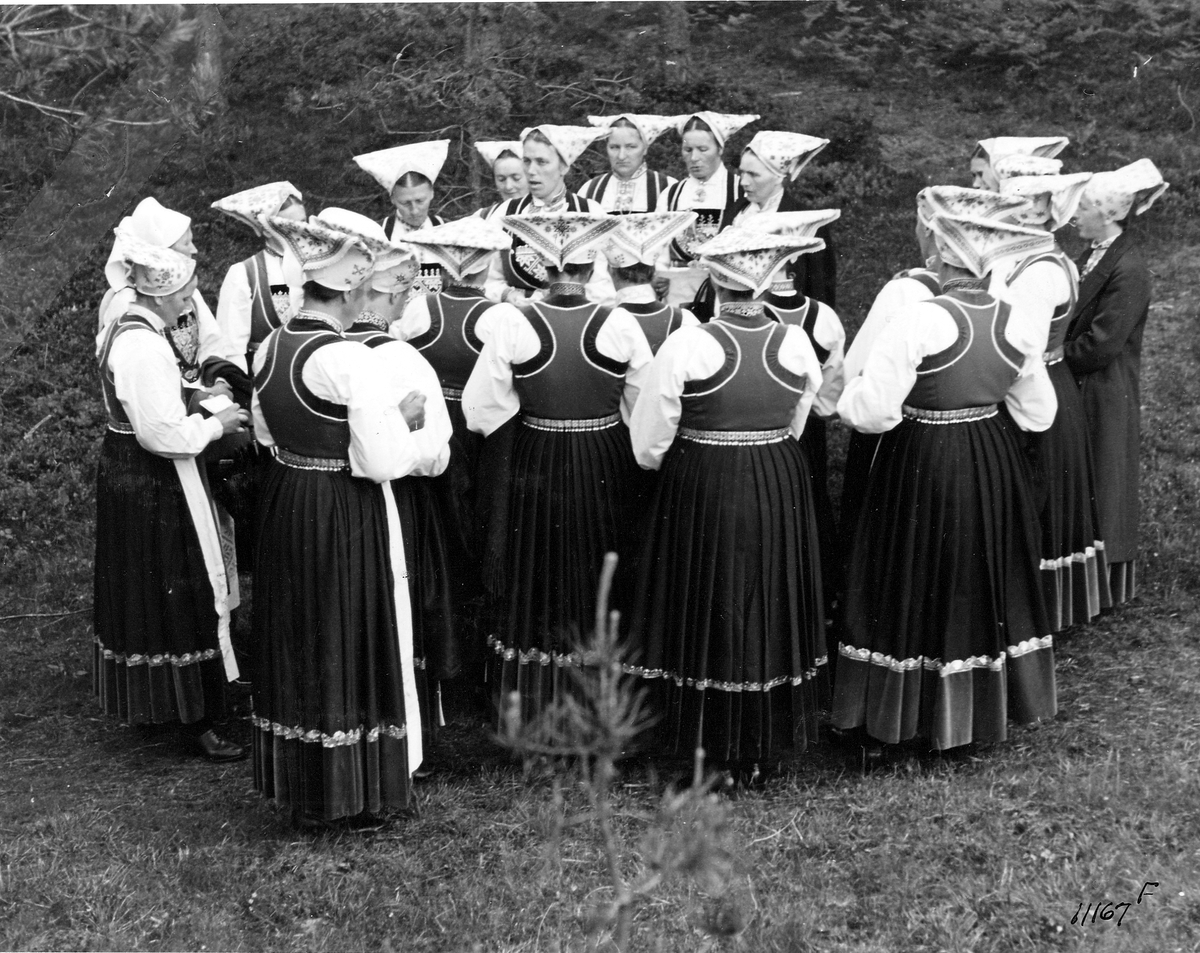 En gruppe kvinner i Vossebunad samlet i en ring på gressbakken.