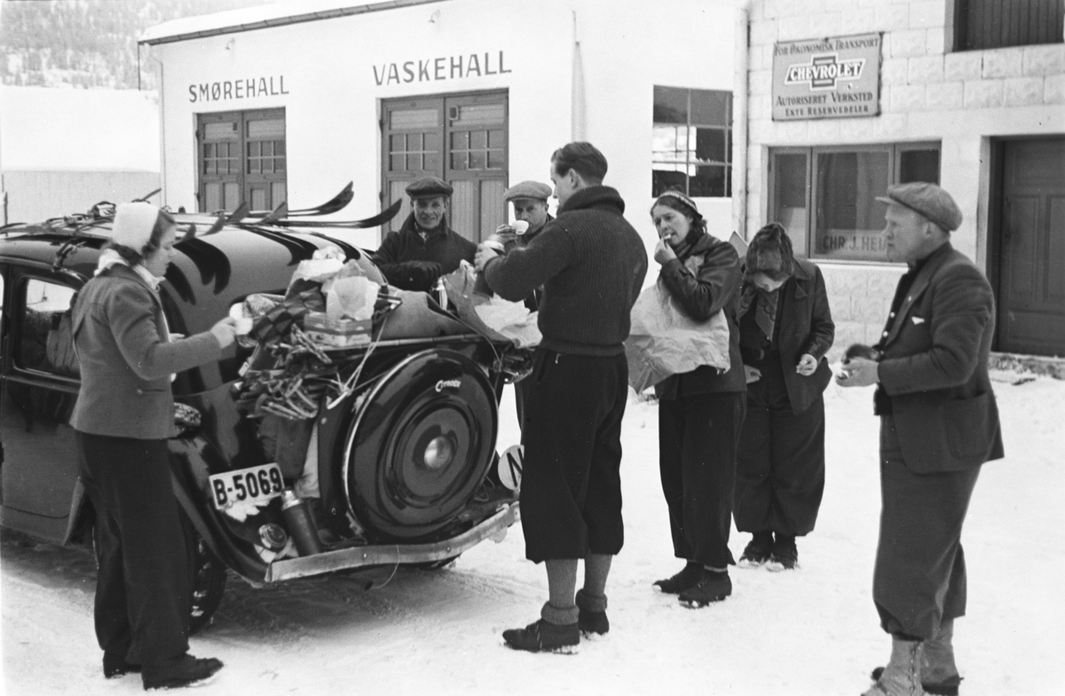Påskefølge tar en pause på bensinstasjonen, tid for mat og drikke.  Skiene er bundet fast på biltaket. Fotografert 1940.