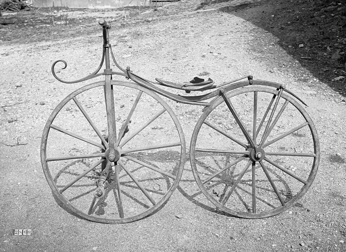 Tvåhjulig cykel med direkt drivning på framhjulet med trampor. Huvudsakligen av trä. Sadeln placerad på den hjulen sammanbindande fjädrande stångens mitt. Märkt: "Husaby" på bakskärmen.