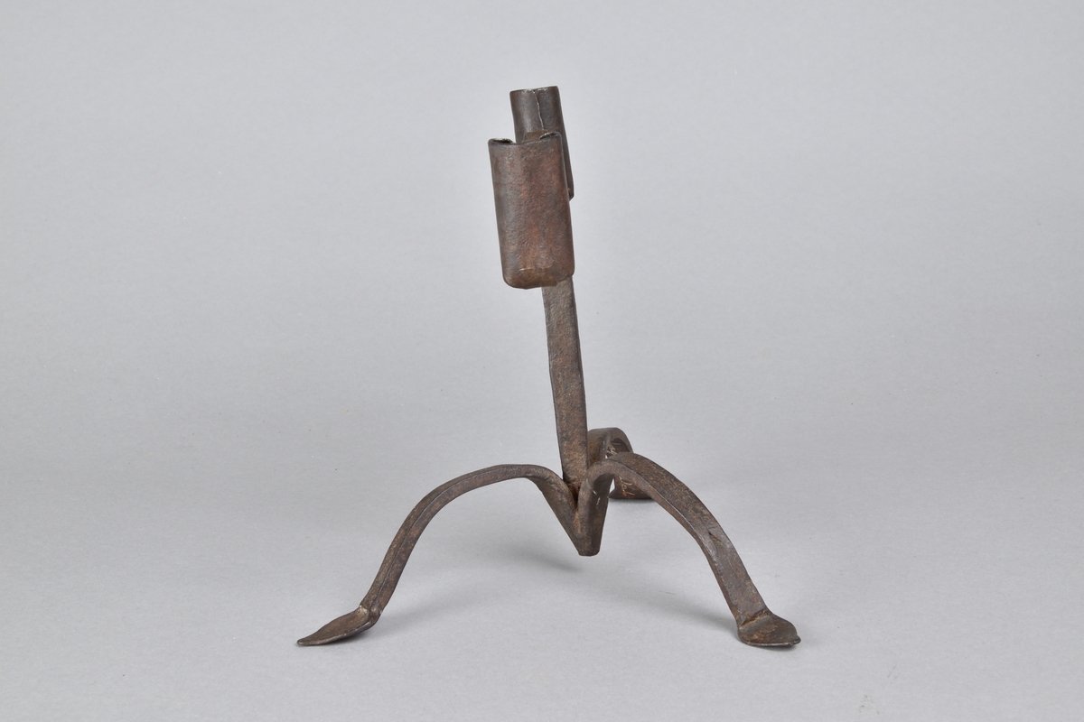 Ljusstake tillverkad i järn. Rak, med två armar och två ljushållare. Tre bågformade ben med bladformade fotavslut. 