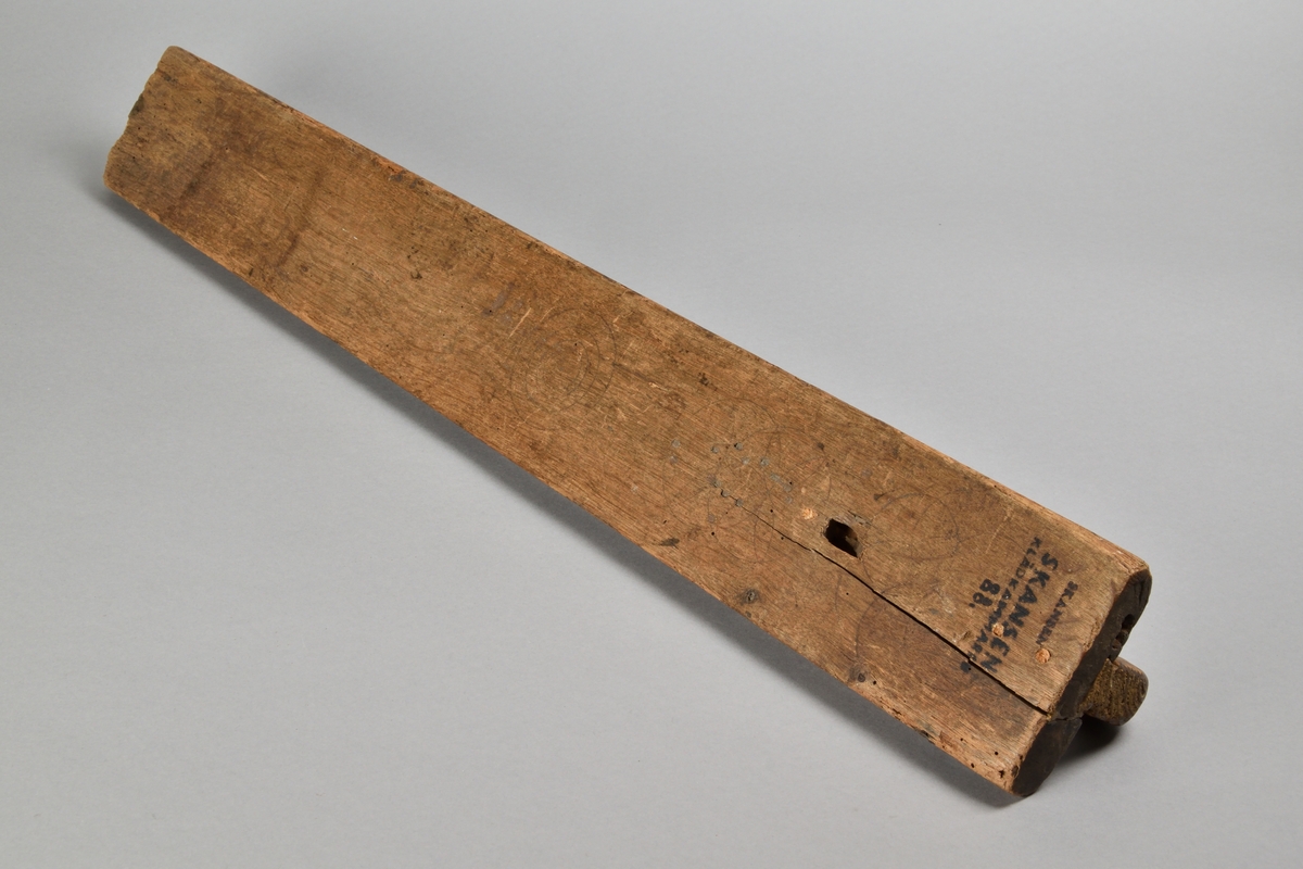 Mangelbräde tillverkat i trä. Rak med profilerade långsidor och handtag av trä. Ovansidan rikt ornerad med skurna mönster, samt inskriften "Anno 1770".
