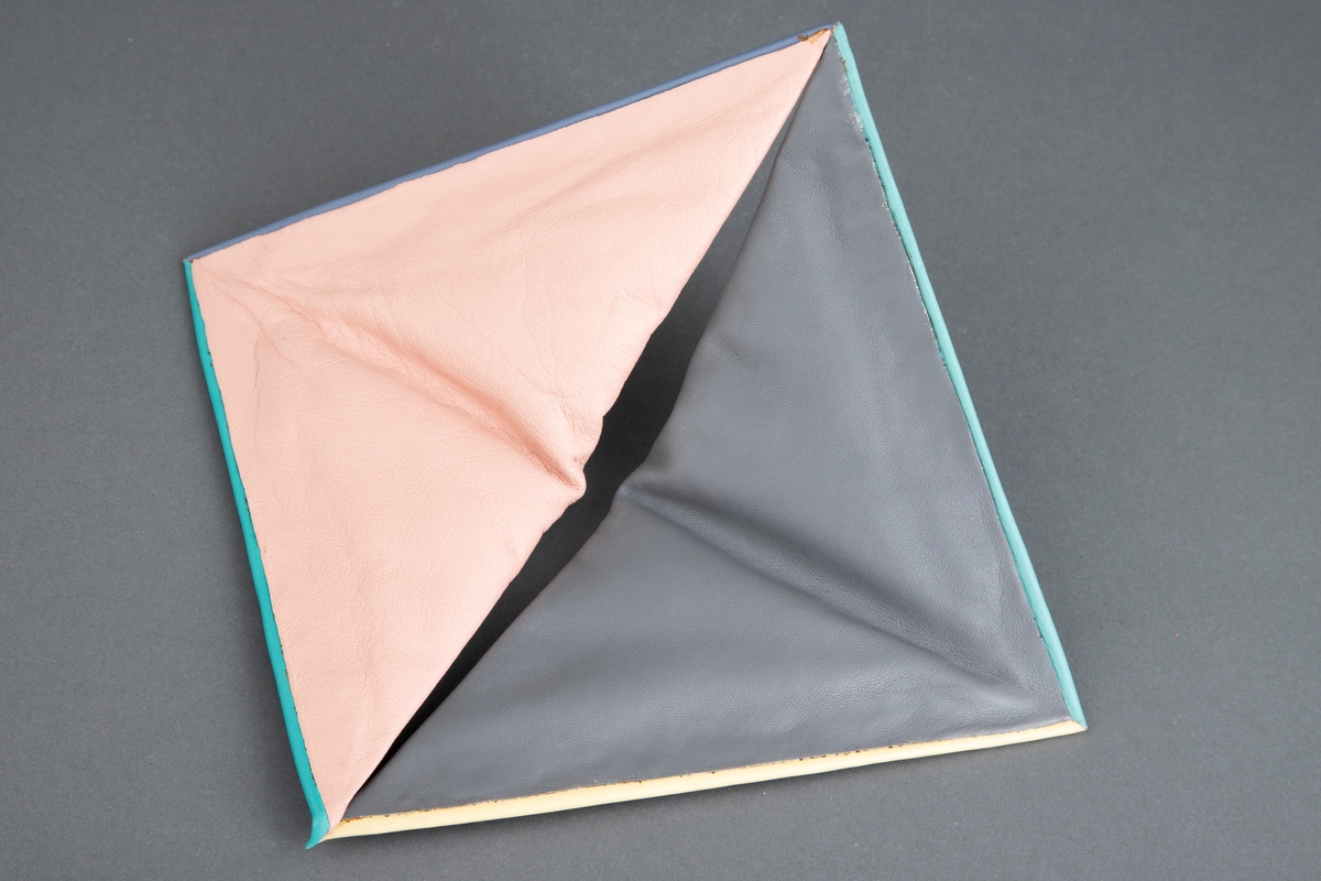 Halskrage bestående av to trekanter i skinn som er festet på en skinntrukket stålskinne, slik at de danner et kvadrat.  Trekantene er i rosa og grått skinn, mens stålskinnene er trukket med grått, grønt og gult skinn. Halskragen kan åpnes i det ene hjørne.