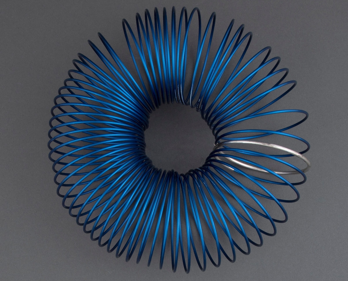 Halssmykke satt sammen av en spiral av blått eloksert aluminium. Ett ledd i spiralen er uført i sølv. Smykket er mykt og føyer seg etter hals og skuldre, men beholder samtidig sin form.