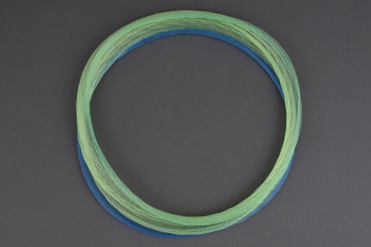 Halsring av nylontråd. Blå, gule og grønne tråder er flettet slik at de danner en elastisk ring som kan trekkes ut til forskjellige former.