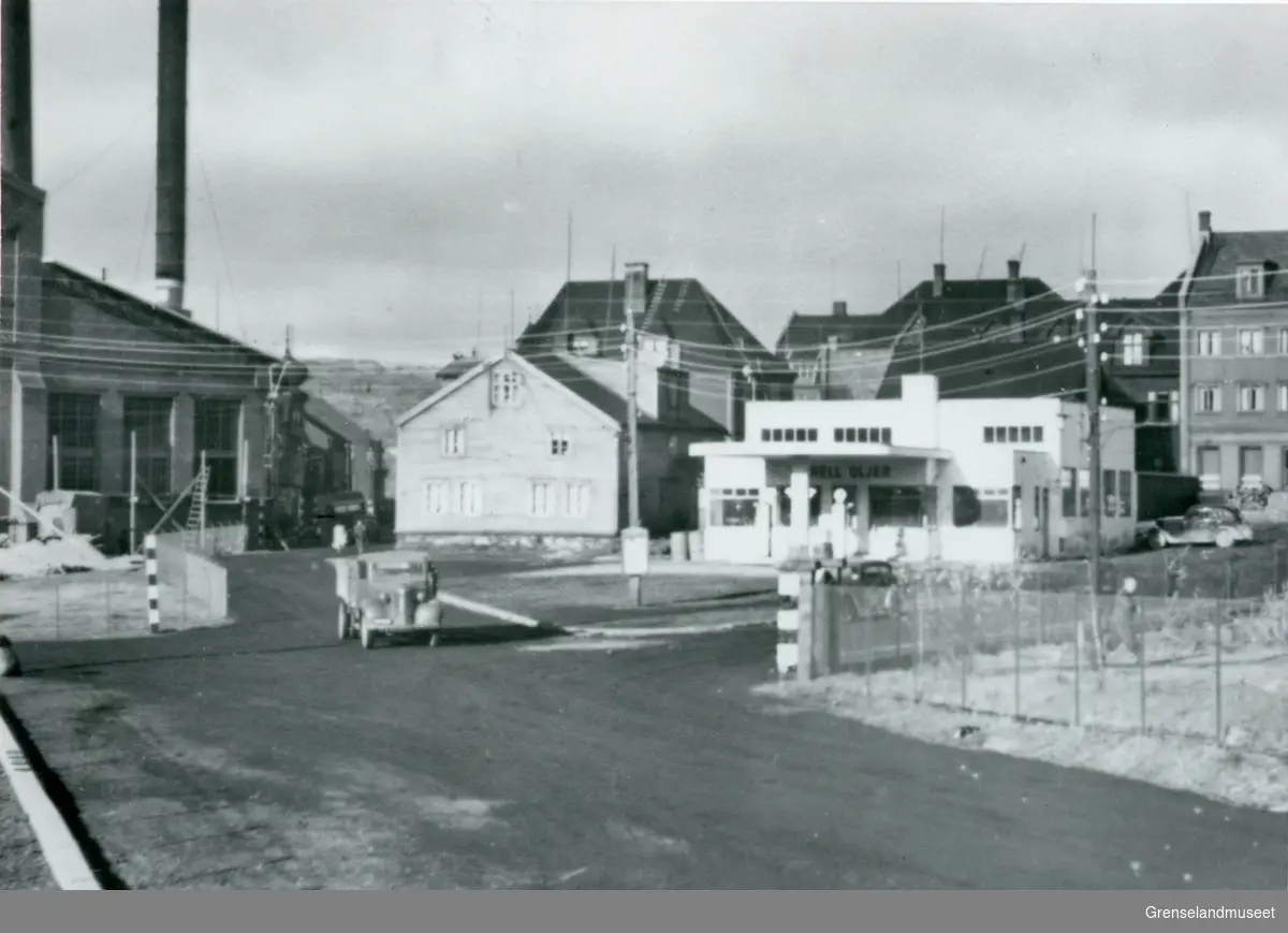 Kirkenes i 1940 etter første bombing 4. Mai. Tyskerne malte markering på utsatte steder langs gatene. Her vises A/S Sydvaranger Dampsentralen til venstre og bensinstasjonen til høyre. Mellom de to er Figenschous gamle bygning. En lastebil kommer kjørende fra Dampsentralen. 