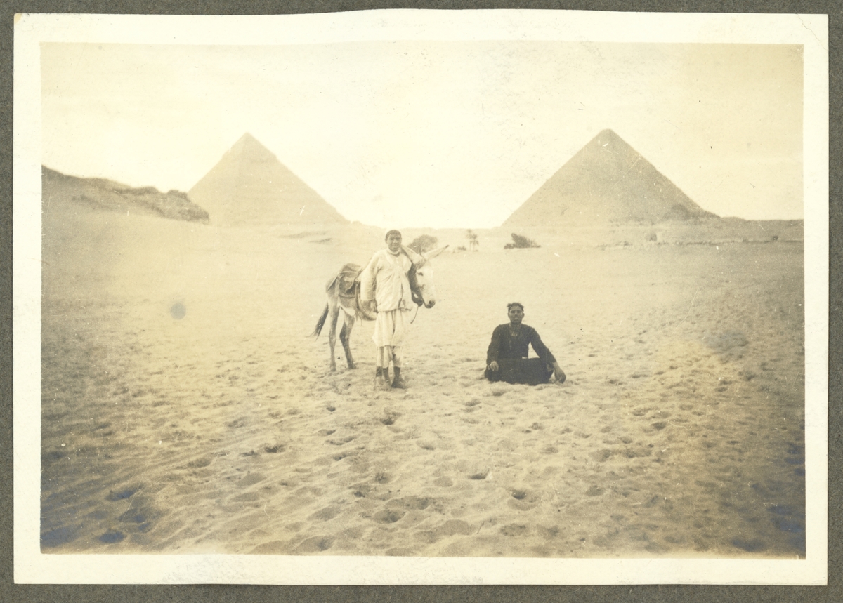 Bilden visar två egyptier som låter sig fotografera framför pyramiderna.