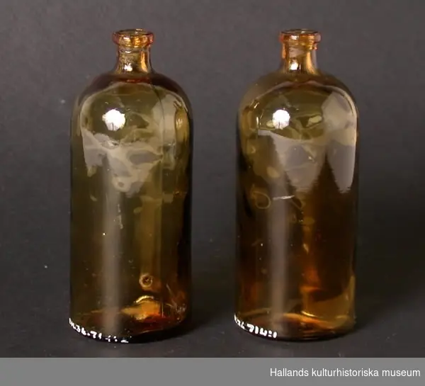 Två flaskor av glas, gulbrun färg, ojämnt gods, cylinderformad.