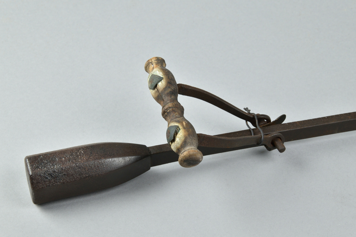 Besman tillverkad i järn. Lång och smal stång med krok i ena änden och åttkantig viktklump i andra änden. Rörligt handtag i järn och trä. Stången med skalor för vikt, och viktklumpen märkt "1779". 