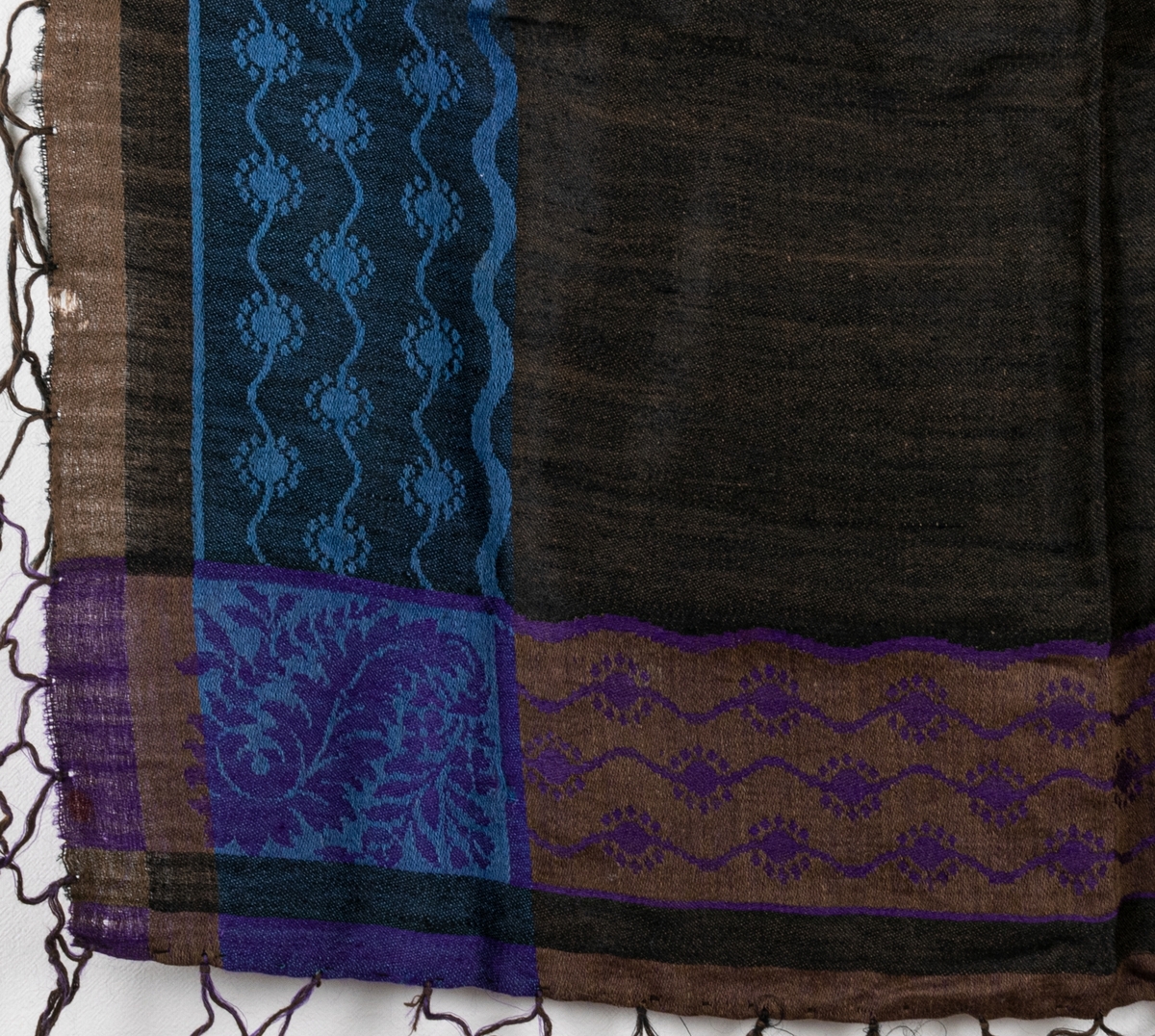 Mångfärgad yllesjal med svar och brun botten med detaljer i lila och blått.