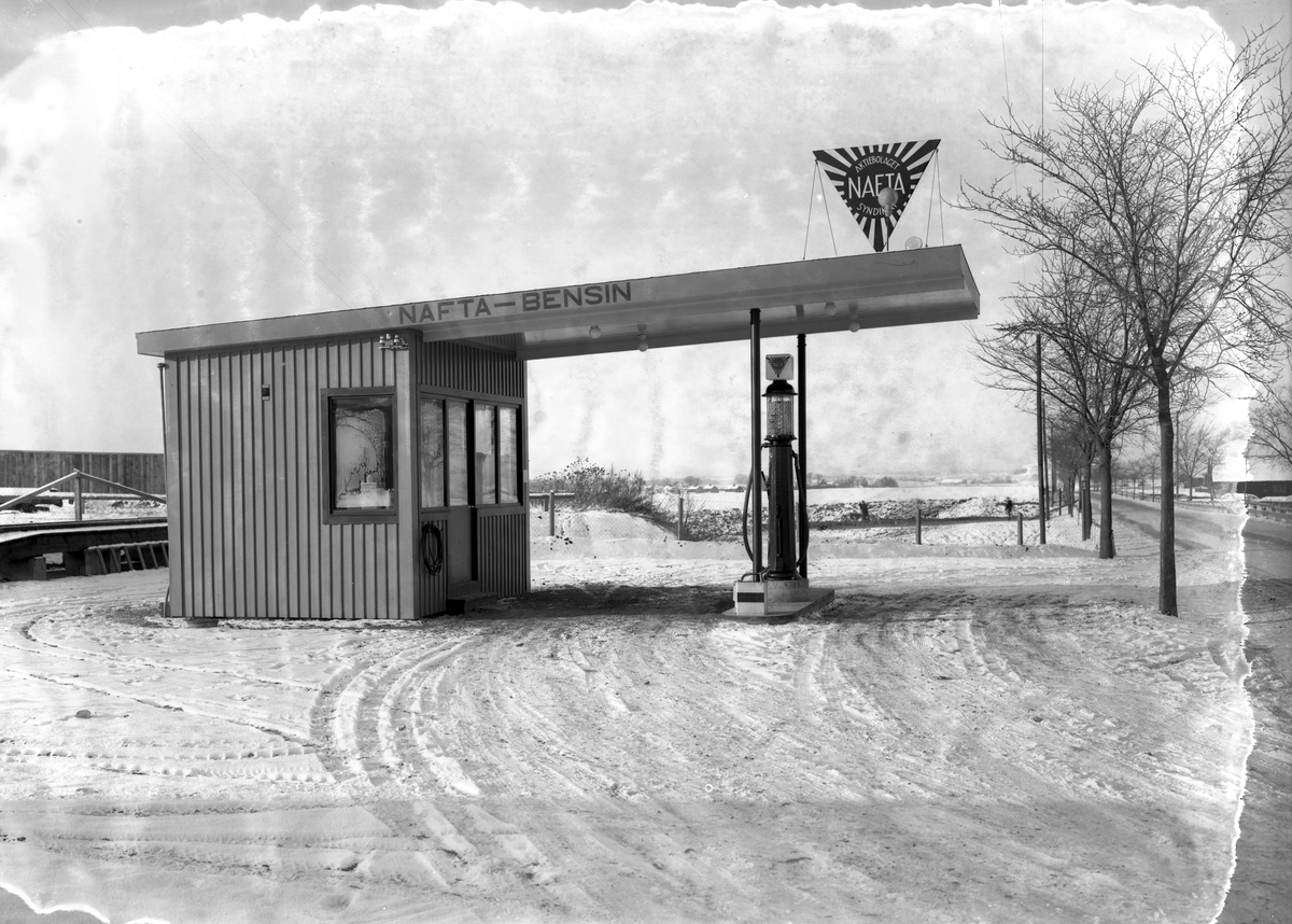 Fotografi som dessvärre inte klarat tidens gång men som detta till trots ger oss en värdefull dokumentation av syndikatet Naftas bensinstation vid Västra vägen-Bergsvägen i Linköping. Bolaget saluförde från 1929 bensin importerad från Sovjet och existerade till Gulf köpte upp företaget 1938. Här en vy mot norr år 1933.