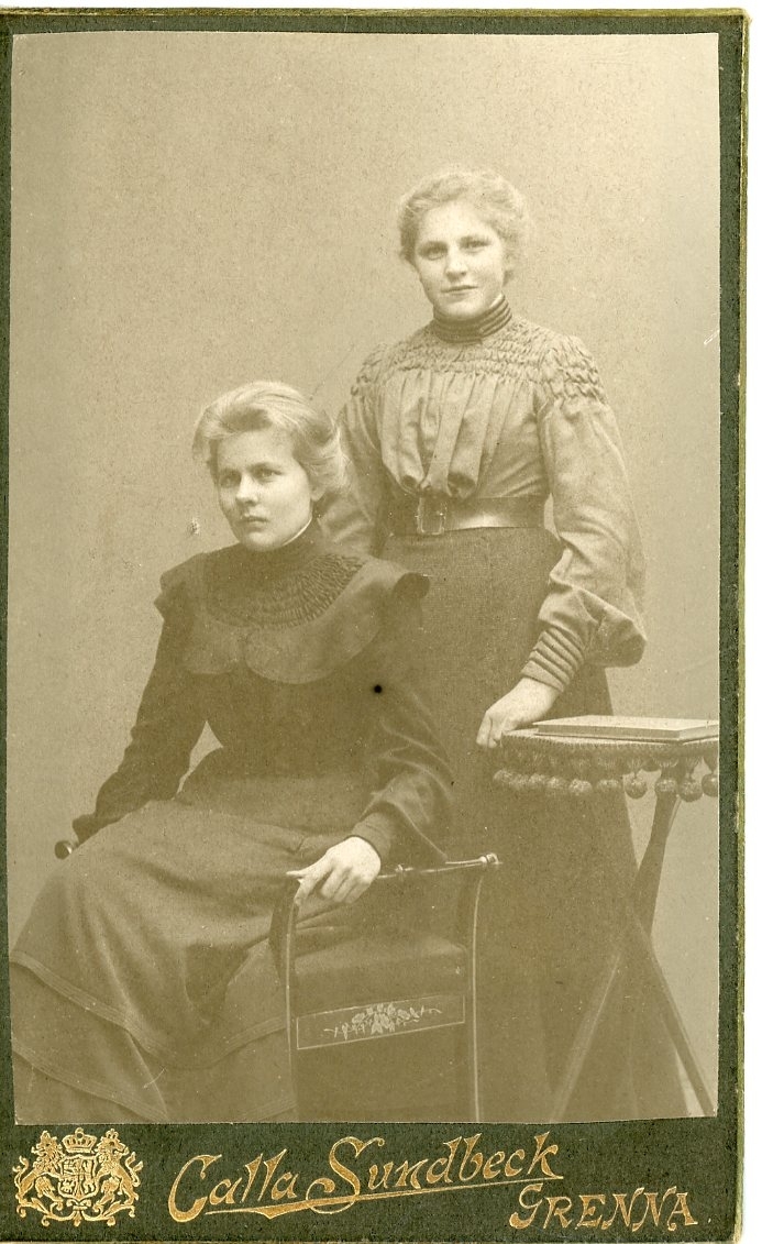 Kabinettsfotografi av två okända unga kvinnor varav en sitter i en stol.
