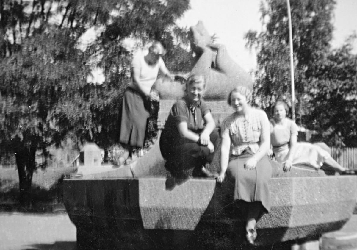 Fire kvinner på ein skulptur i ein by.