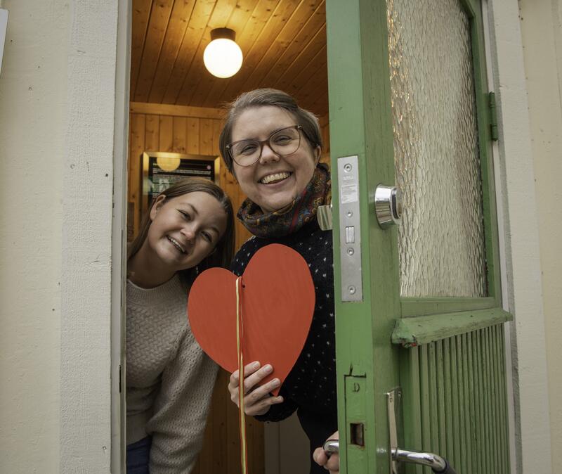 To jenter står i døra og ønsker velkommen inn. Den ene holder et hjerte i hånden. (Foto/Photo)