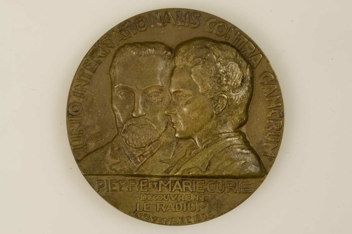 Motiv advers: Pierre og Marie Curie, byster, han frontal, hun i profil mot venstre.