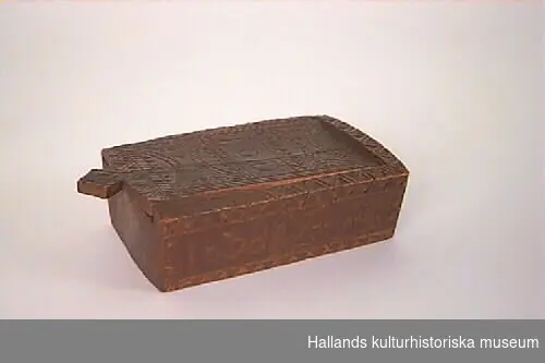 Lådan är skuren i ett stycke och har skjutlock. Den är rikt dekorerad i ristnings- och karvsnittsteknik, samt målad rödbrun. Märkning på locket IOD och på långsidan 1838.