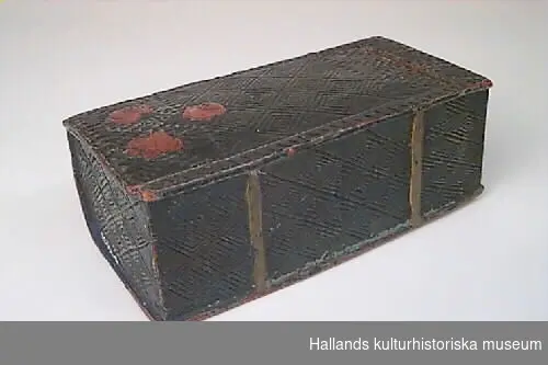 Bokfodral i form av en bok. Asken är snidad i ett stycke och har skjutlock som löper i en fals. Asken är dekorerad med romboidiska mönsterfält i ristningsteknik och med uddsnittsbårder. Asken är bemålad senare eller ommålad i grönt med ryggfalsar i rött och fläckar av blått. På ryggen är ristat "BTS" och målat "1863 CAAS". 