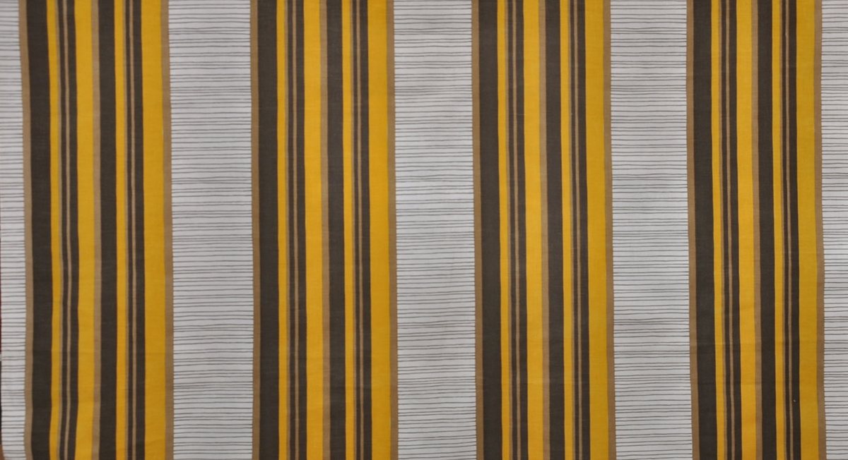 Tryckt bomullstyg, 1950-tal.
Originalbredd 120 cm. Gardintyg, BW7430 design 6902-2. Långrandig i gult, brunt, beige. Tvärgående smala gröna ränder på oblekt botten.
Mönsterrapport 32 cm.
Otvinnat garn.
