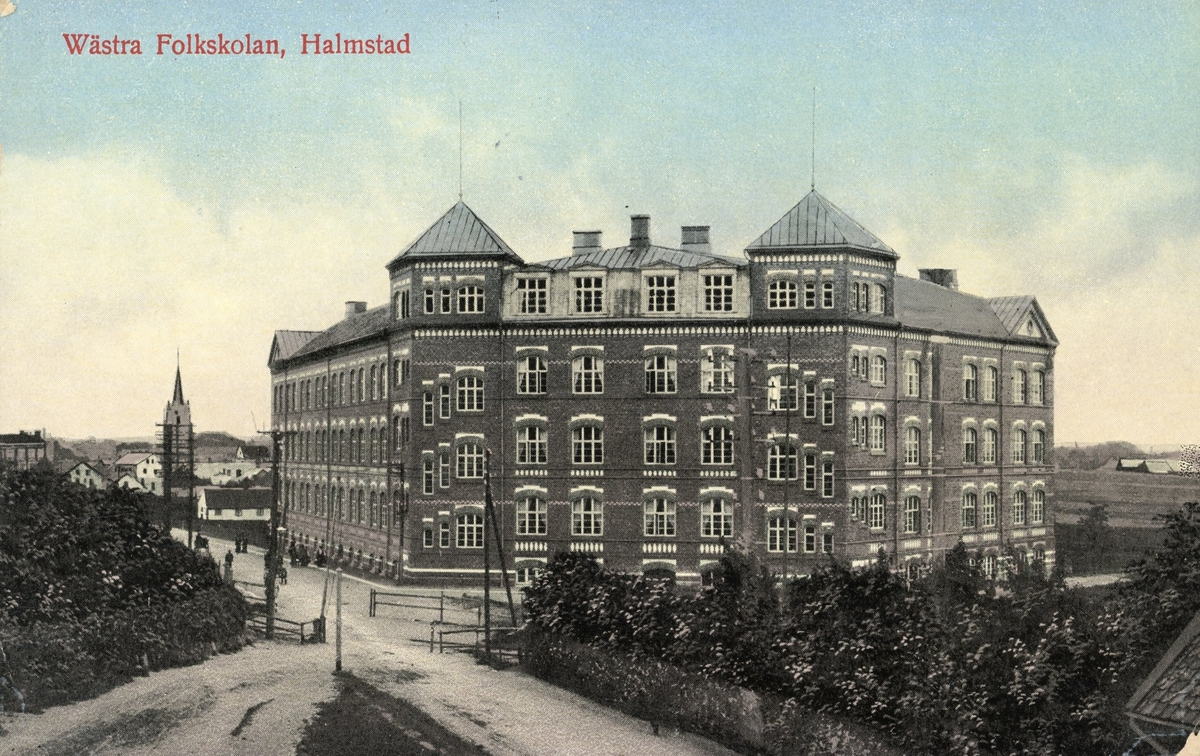 Kolorerat vykort, "Wästra Folkskolan, Halmstad", stämplat 1916. Skolbyggnaden ritades av dåvarande stadsarkitekten Sven Gratz (1864-1931) och invigdes 1908. Det sägs att Sven Gratz hade låtit sig inspireras av Lunds domkyrka och därför försåg den gedigna tegelbyggnaden med två torn. På 1930-talet började skolan kallas för Brunnsåkerskolan, eftersom platsen den byggts på hade benämnts som Brunnsåkern, eller Olssonska lyckan. (Se även bildnr F9264)