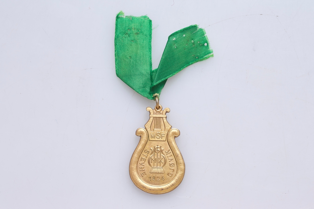 Medalje formet som en harpe. Dekoren er tre ulike varianter av en harpe.