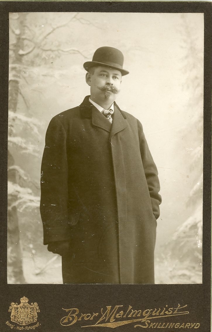 Kabinettsfotografi av en okänd man med skägg. Han bär ytterkläder och hatt.