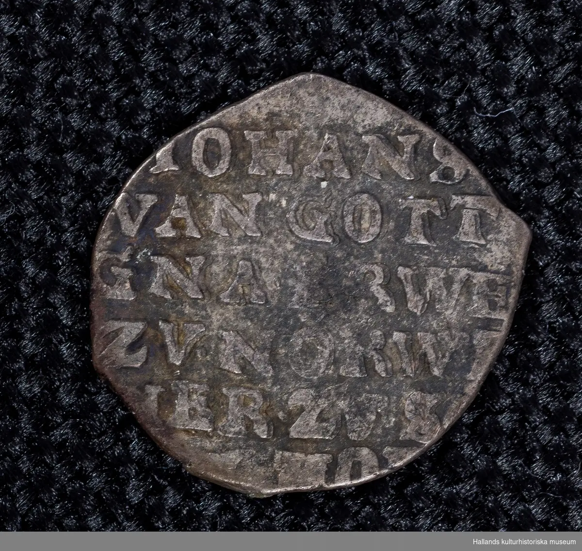 Arkeologiskt föremål. Holländskt silvermynt. Präglingsår 1675.På ena sidan överst präglingsåret. under sköld av en krona, omgiven av en strålkrans och två pilar. På ömse sidor bokstäverna "Z" och "L". På motstående sida följande text: "JOHANS VANGOTT GNA...RWE ZV. NORW  IER ZVS" Myntet är sönderklippt. 