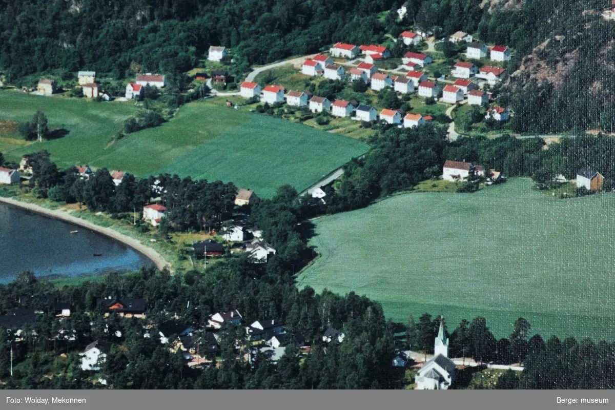 Flyfoto av Berger sett fra øst. Man ser odden med Berger brygge, kirken, stranda, idrettsplassen, hovet, øvre og nedre gate og litt av boligene i Kleiva og en liten bit av Fossekleiva fabrikkanlegg. 