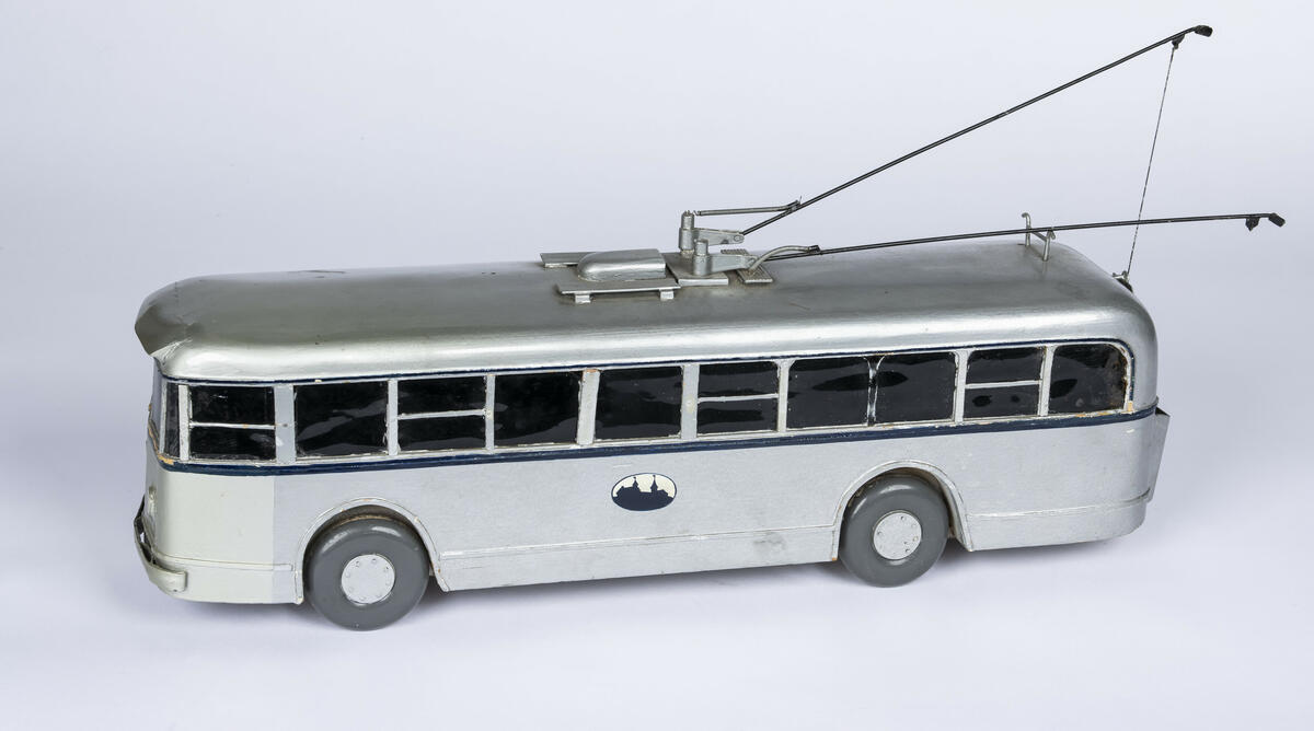 Modell av tre av buss A-1577. Bussen er farget i en sølvfarge med en mørk blå stripe på midten som går rundt hele modellen. Vinduene er farget sorte og de fire dekkene av tre er i en mørk grå farge. Bussen har tre inngangs- og utgangsdører. Denne modellen har to trolleystenger med kontakssko på enden og to trolleystenger som er festet til to snorspoler på baken av bussen. På enden av taket er det også plassert kroker for å feste trolleystengene når når ikker er i bruk.