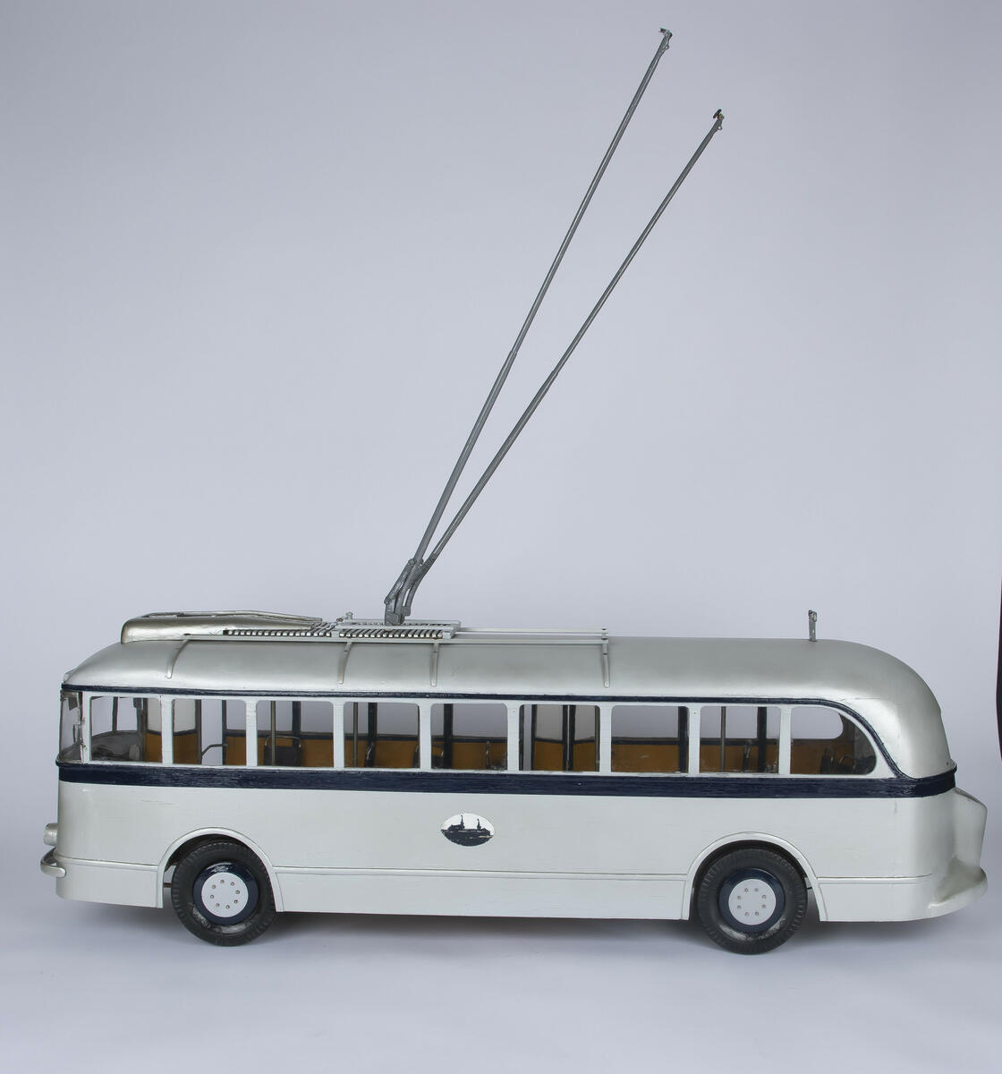 Tremodell av trolleybuss A-15700 med fungerende hjul og inngangs- og utgangsdører. Modellen er farget sølv med en mørk blå stripe som går rundt hele modellen langs midten, samt andre dekorative elementer. Modellen har to fungerendee fjærbelastede trolleystenger/strømavtagere på taket og kroker som stengene kan hektes på på bakre del av taket til bruk hvis bussen må taues. Interiøret består av okergule vegger og enkeltseter i en brun farge.