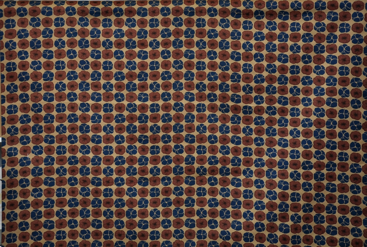 Bomullstyg, början av 1960-talet.
Klänningstyg på 90 cm bredd. Tryckt mönster med mörkbruna och blå violer på beige botten som är styckfärgad före tryck.
Otvinnat garn.
Rapport 10,5 x 11,5 cm.
Tryckfärger 3.1