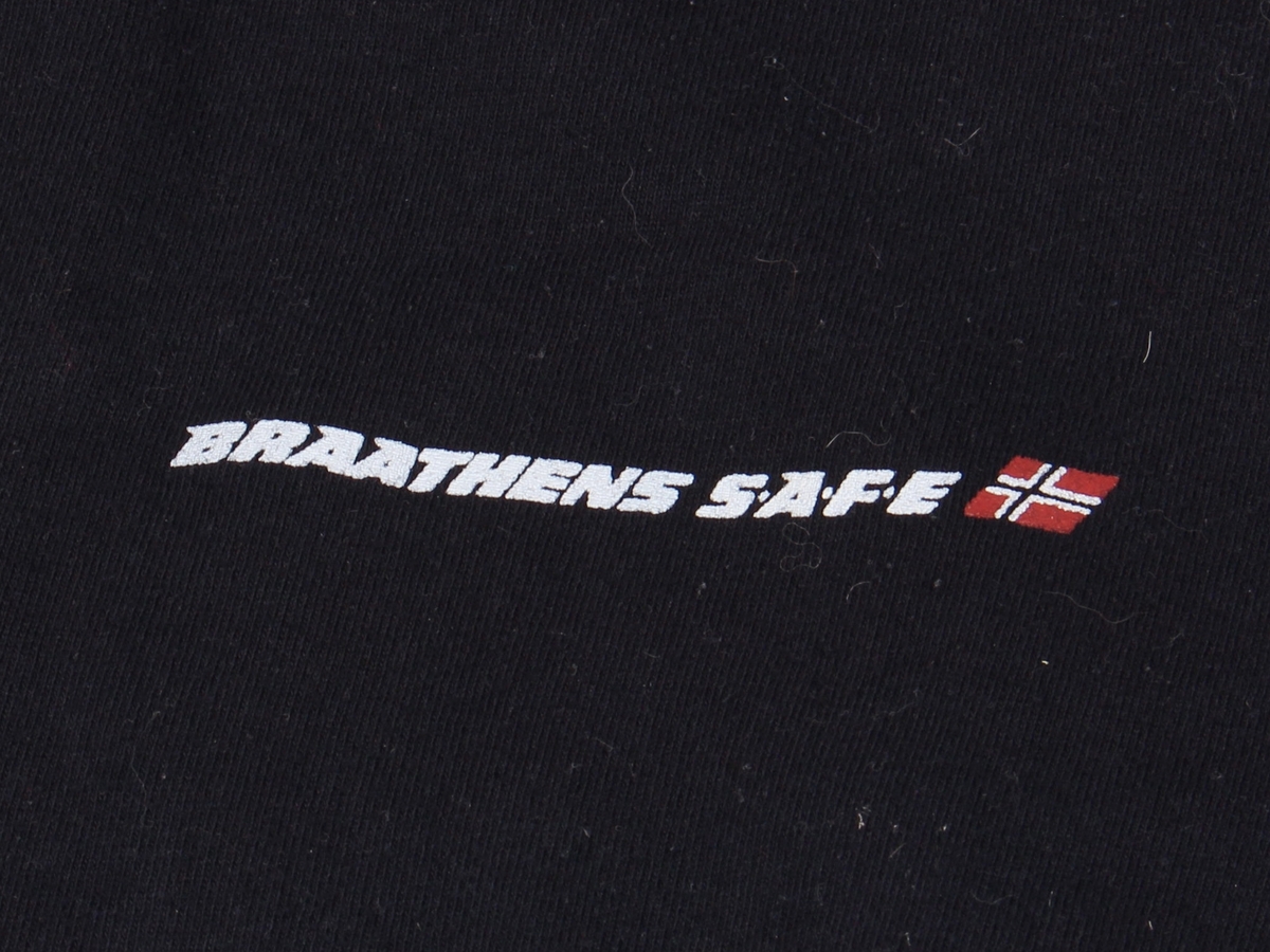 Mørk blå genser med glidelås i hals. Braathens SAFE-logo på brystet og påtrykt rundt merke på venstre erme, samt påskrift på ryggen. Størrelse L.