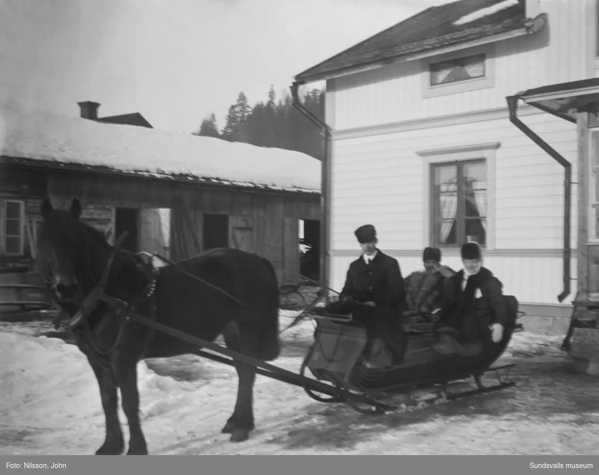 En häst spänd framför en släde på gården Roken 1:7 i Laggarberg. I släden sitter två män och en kvinna, en av männen är klädd i vargskinnspäls.