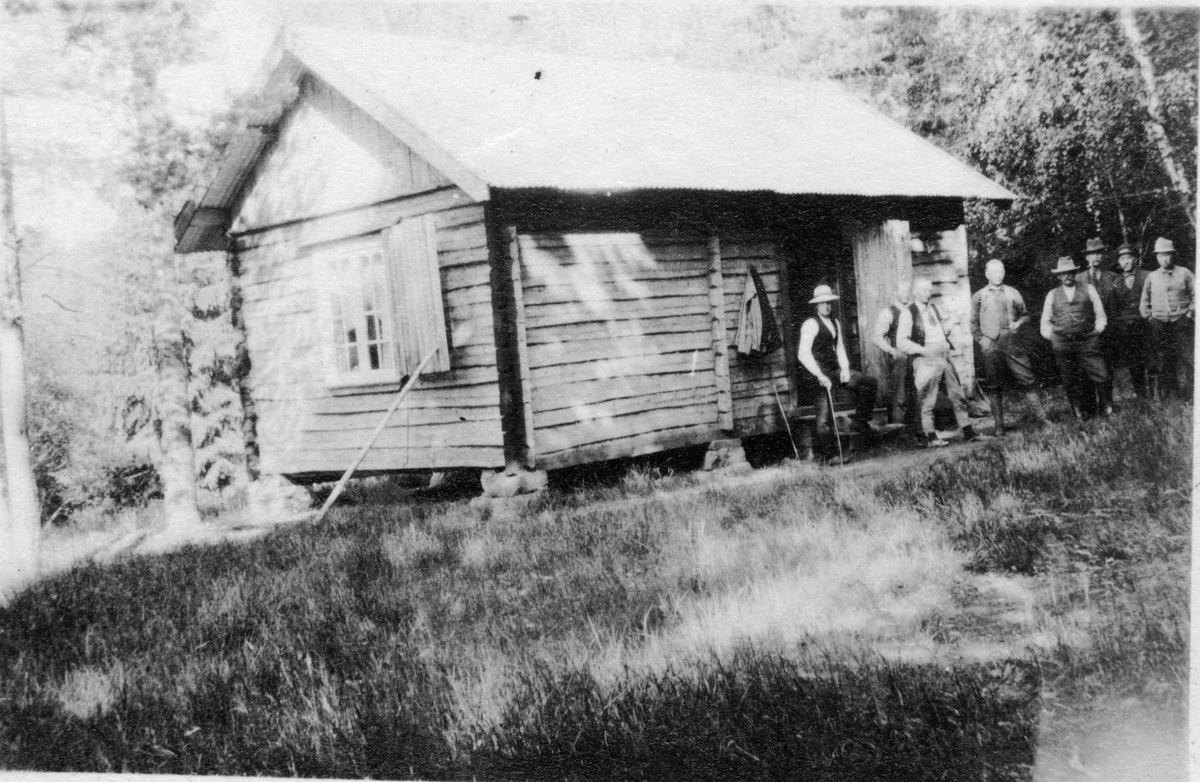 Portrett av en gruppe menn foran mindre hus.