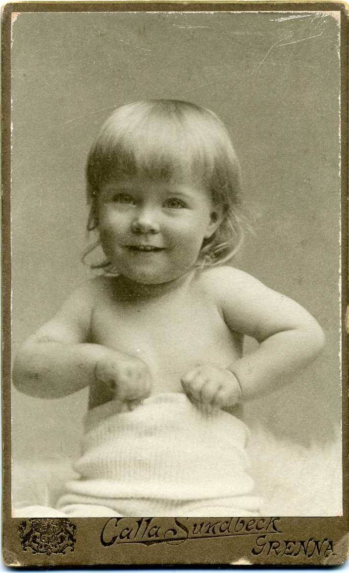 En litet barn med bar överkropp sitter på en ljus skinnfäll.