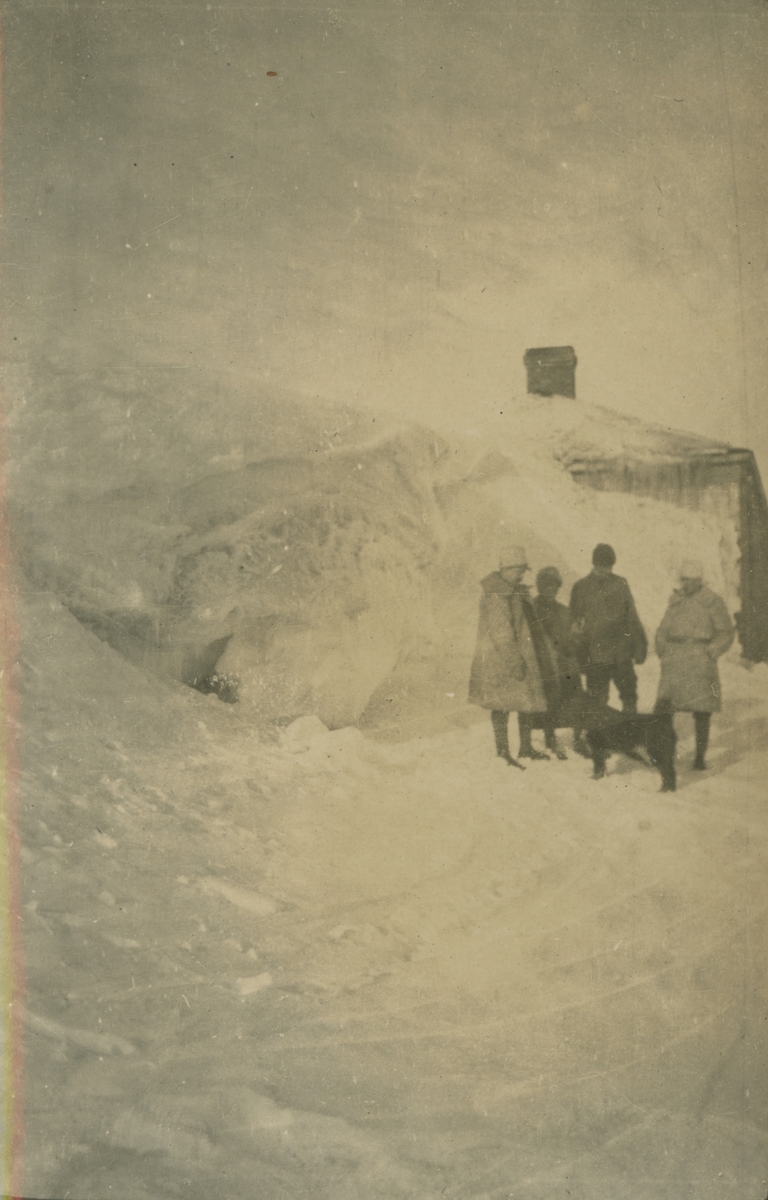 Fotografi från expedition till Spetsbergen. Motiv av expeditionsdeltagare och hund i snön framför hus.