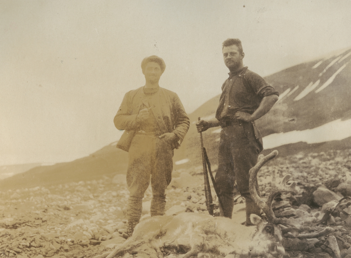 Fotografi från expedition till Sveagruvan. Motiv av två män som poserar vid död ren. En av männen håller i ett gevär.